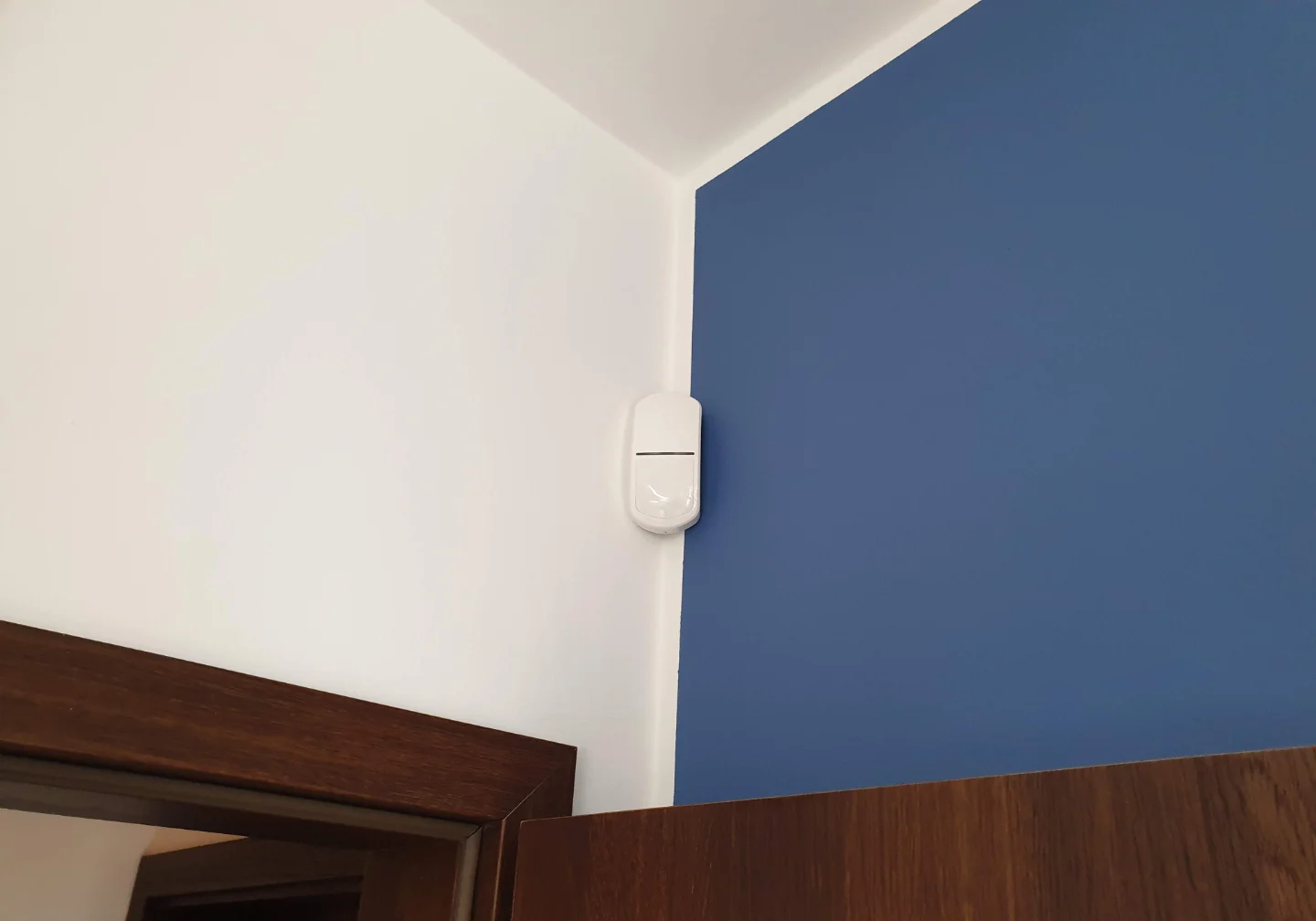 Biały czujnik ruchu Satel SLIM zamontowany na ścianie w salonie – dyskretny system alarmowy Winkam Rybnik.