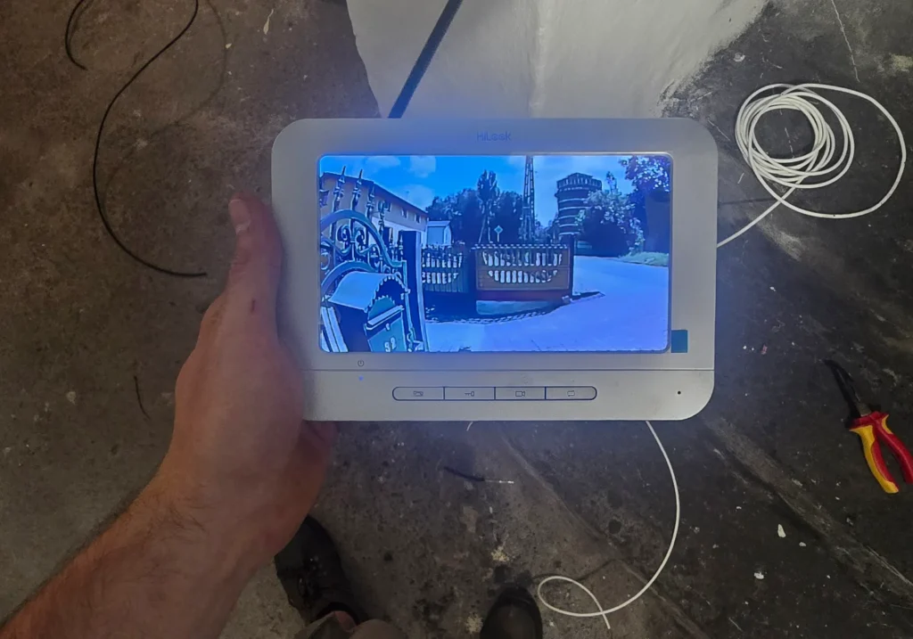 Instalator Winkam trzyma włączony monitor wideodomofonu HiLook podczas konfiguracji – widoczny wyraźny obraz ze stacji bramowej.